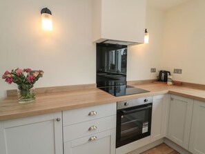 A modern kitchen with a built-in oven, a microwave, and a stainless steel range hood. There are two wall-mounted light fixtures and a vase with flowers on the countertop. - Gudhjem, Seahouses, Sleeps ten (Seahouses)