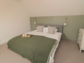 A neatly made bed with a green throw blanket, a bedside table with a lamp, and a dresser. - Gudhjem, Seahouses, Sleeps ten (Seahouses)