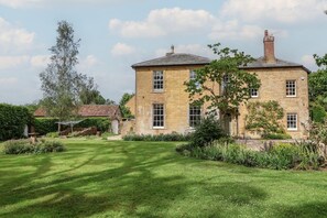 Une maison en pierre à deux étages, dotée d’une pelouse et d’un jardin bien entretenus.