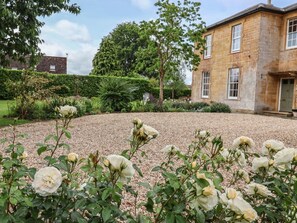 Un jardin avec des rosiers blancs, un chemin de gravier et un bâtiment en pierre doté de fenêtres.