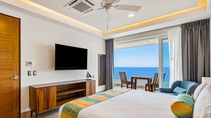 Quarto de hotel com cama, televisão, escrivaninha e vista para o oceano.