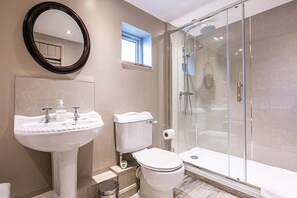 Un baño con lavamanos blanco, inodoro y ducha con mampara de vidrio.