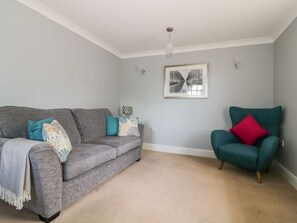 A living room with a grey sofa, teal armchair, and a framed picture on the wall. - The Hoist: Modern Living in Ely (Ely)