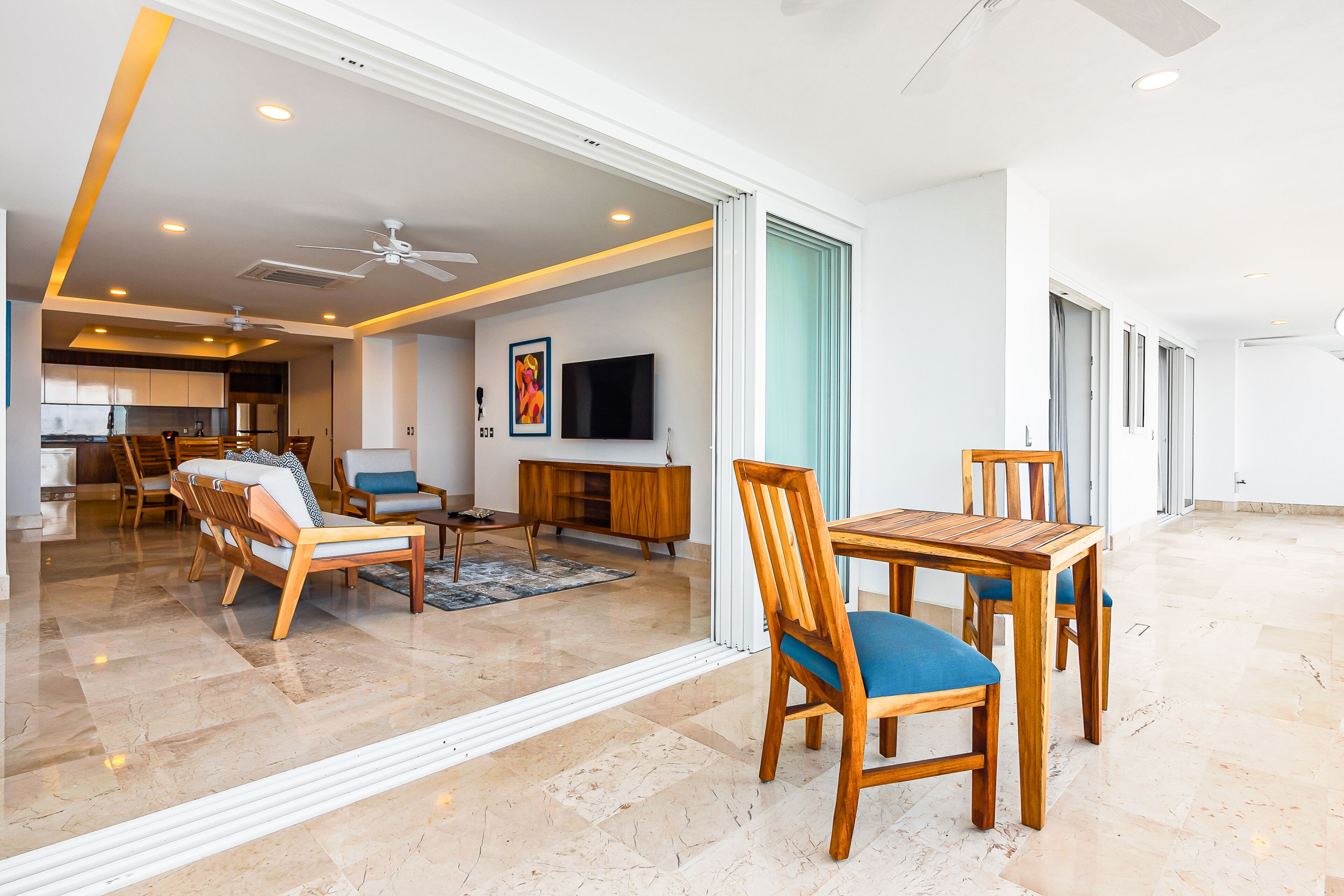 A spacious living area with a dining table and chairs, a sofa, and a TV mounted on the wall.