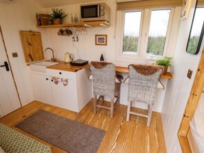 A compact kitchen with a microwave, sink, and two wicker chairs. - Shepherds Hut - Ash, Lincoln (Lincoln)