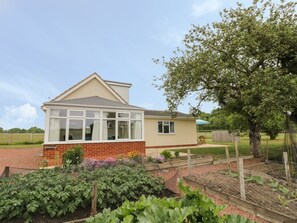 A house with a conservatory, a brick base, and a garden with raised beds. - Buttercups at Midway, Kington (Worcester)