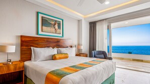 Una camera d'albergo con un letto grande, vista sul mare, un quadro appeso al muro e una poltrona vicino alla finestra.