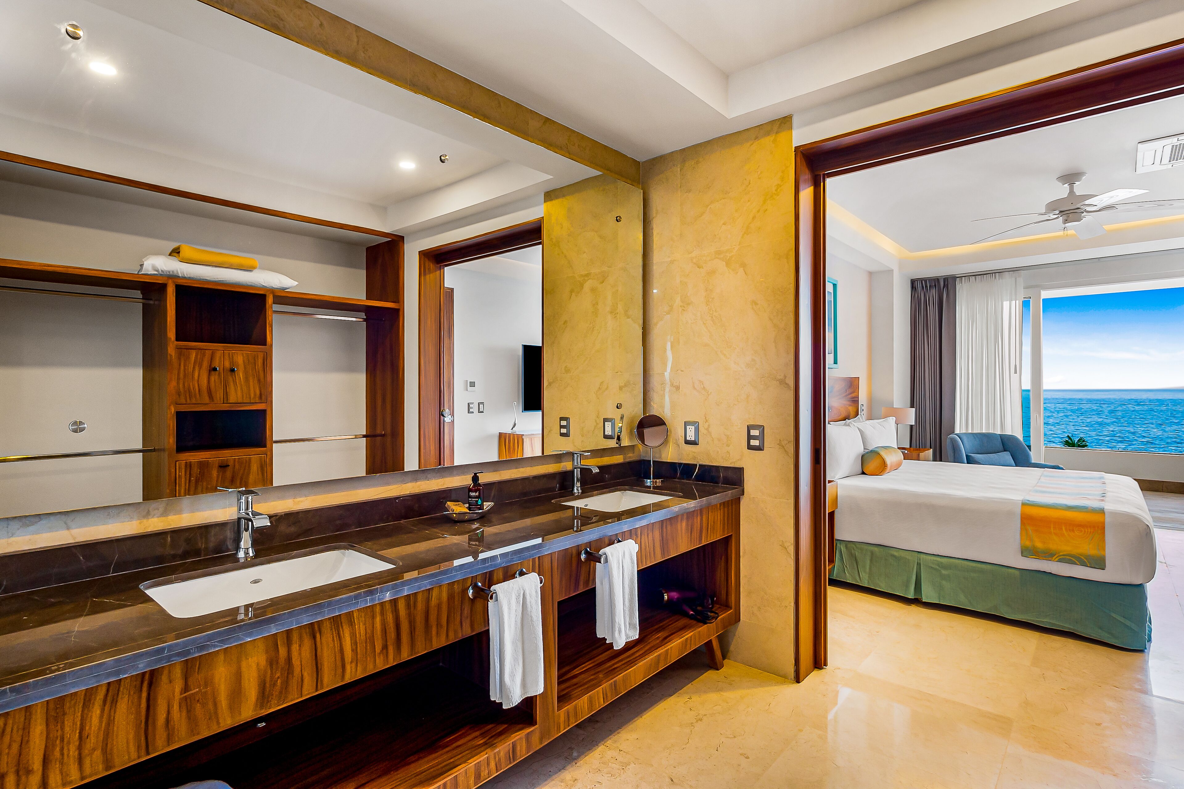 Quarto de hotel com toucador de madeira, um espelho grande, cama com vista para o mar e varanda.
