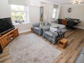 A living room with a sofa, TV, wooden entertainment unit, and a dining area with a table and chairs.