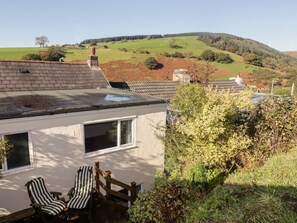 A house with a sloped roof, a wooden fence, and a view of rolling hills.