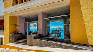 Ein moderner Hotel Eingang mit Glasfassade, Sitzgelegenheiten im Freien und Blick auf das Meer.