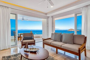 A modern living room with a sofa, armchairs, and a coffee table. Large windows offer a view of the ocean and a distant island. - Blue Horizon 701 | 1BR/2BA in Puerto Vallarta, Ocean View, Pool & Gym (Puerto Vallarta)