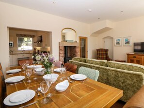 A dining area with a wooden table set for four, a sofa, a fireplace, and a television in the background. - The Card House, Hopton (Matlock)