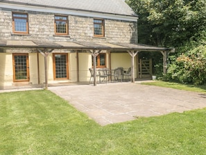 A stone building with a covered patio area, a table and chairs, and a small garden.