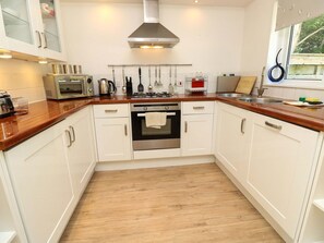 A kitchen with white cabinets, a stainless steel range hood, a built-in oven, and a window with a view. - Whitfield P1, Yarmouth (Yarmouth)