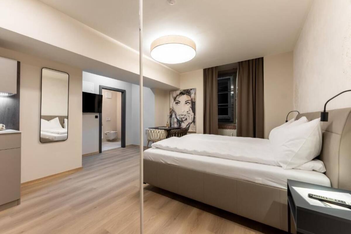 A modern hotel room with a large bed, a mirror, a desk, and a painting on the wall.