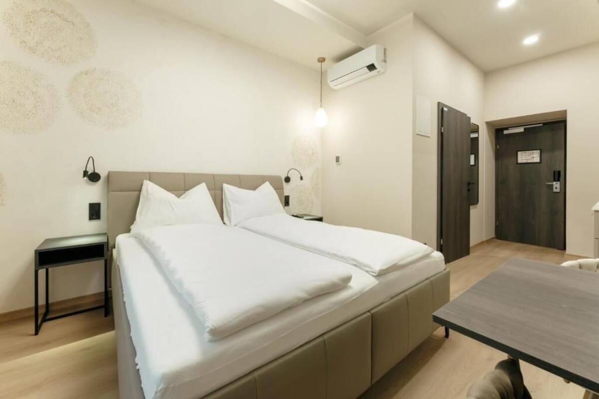 A double bed with a headboard, a bedside table, an air conditioning unit, a door, and a small table.