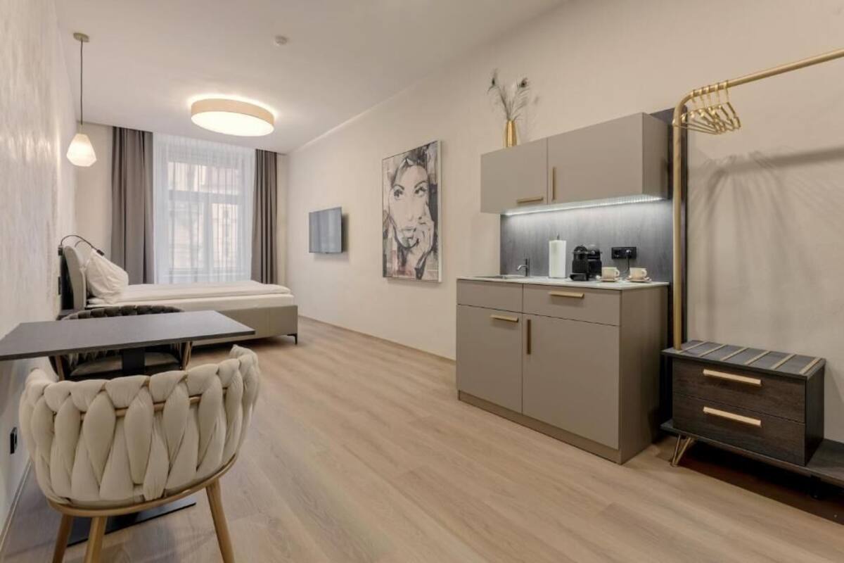 A modern hotel room with a bed, a dining table, a kitchen area, and a seating area.