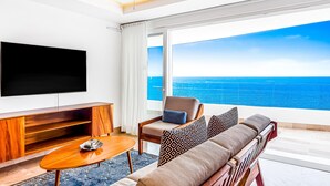 A modern living room with a large TV, a sofa, a chair, and a view of the ocean. - Ocean-view Puerto Vallarta condo with pool, gym (Puerto Vallarta)