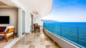 A balcony with a view of the sea, a flat-screen TV, and a seating area with chairs and a table. - Ocean-view Puerto Vallarta condo with pool, gym (Puerto Vallarta)