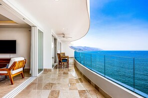 A balcony with a view of the sea, a flat-screen TV, and a seating area with chairs and a table. - Ocean-view Puerto Vallarta condo with pool, gym (Puerto Vallarta)