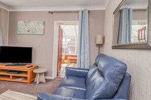 A living room with a leather sofa, a flat-screen TV, a small table, and a painting on the wall. - Echo Beach, Seasalter (Whitstable)