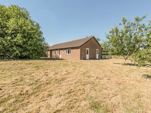 A single-story brick building with a pitched roof, a door, and windows, surrounded by a grassy field and trees.