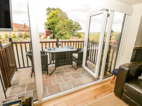 A room with a sliding glass door leading to an outdoor patio with a table and chairs. - The Hayshed, Hawsker (Whitby)