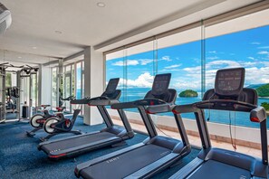 Un gimnasio con cintas de correr y equipo de ejercicio, amplias ventanas con vista al mar.