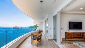 A balcony with a view of the sea, a dining table, chairs, a TV, and a wooden cabinet. - Blue Horizon 804 | 2BR/2BA Puerto Vallarta | Ocean View, Pool, Gym (Puerto Vallarta)