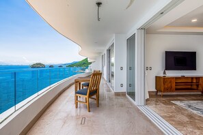 Ein Balkon mit Meerblick, einem Esstisch, Stühlen, einem Fernseher und einer Holzkommode.