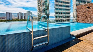 A rooftop infinity pool with a metal ladder, surrounded by high-rise buildings and a clear sky. - Ocean-view Portosanto 502 in Puerto Vallarta, 2BR/2BA (Puerto Vallarta)