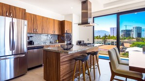 A modern kitchen with stainless steel appliances, wooden cabinets, and a large island with bar stools. - Ocean-view Portosanto 502 in Puerto Vallarta, 2BR/2BA (Puerto Vallarta)