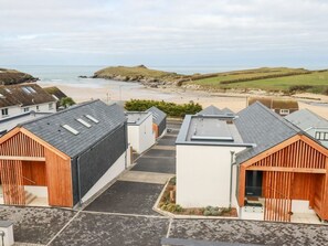 A coastal residential area with modern houses, a beach, and hills in the background. - Porth Beach Villa 9 Longshore, Newquay (Newquay)
