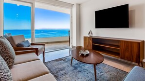 Ett modernt vardagsrum med en stor TV, en soffa, ett soffbord och utsikt över havet genom stora fönster.
