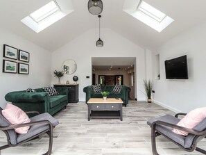 A spacious living room with a high ceiling, two green sofas, a wooden coffee table, and a TV mounted on the wall. - Charming Ty Coch in Ruthin (Ruthin)