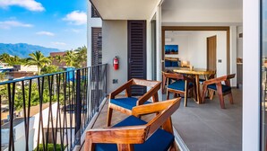 Un balcon avec des chaises et une table en bois, d’où l’on peut admirer un paysage urbain dominé par des montagnes.