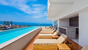 Un espace aménagé au bord de la piscine, avec des chaises longues et une vue sur l’océan et le paysage urbain.