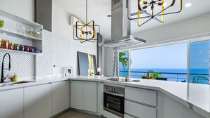 A modern kitchen with white cabinetry, a built-in oven, and a large window overlooking the sea. - Dog-friendly ocean view penthouse & studio with a full kitchen & kitchenette (Puerto Vallarta)