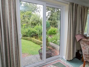 A room with a sliding glass door leading to a garden, a patterned rug, and a chair with a floral cushion. - Crosby Cottage, Wooler, 3 bed. (Wooler)