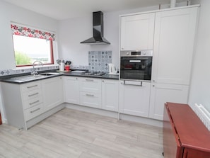 A modern kitchen with white cabinets, a gas stove, a built-in oven, and a window with a floral curtain. - Crosby Cottage, Wooler, 3 bed. (Wooler)