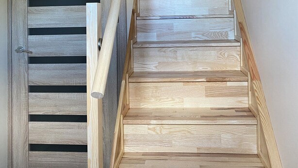 Un escalier en bois, doté d’une rampe, mène à une porte ornée de lattes horizontales.