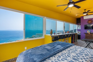 A room with a large window, a bed, a ceiling fan, and a bar area. - Gardenias Studio | Studio in Puerto Vallarta with panoramic views (Puerto Vallarta)