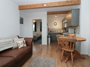 A living room with a brown leather sofa, a wooden dining table with chairs, a kitchen with grey cabinets and a microwave, and a patterned rug on the floor. - Little Winder, Askham, Cumbria (Penrith)
