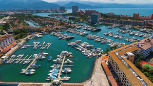 Un port de plaisance où sont amarrés de nombreux bateaux, entouré de bâtiments et avec des montagnes en arrière-plan.