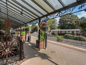 A covered outdoor area with a vintage metal structure, potted plants, and a train in the background. - Bryn Tawel in Penmachno, Conwy (Betws-y-Coed)