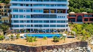 A multi-story hotel with a pool, surrounded by rocks and palm trees. - Blue Horizon 601 | 1BR/2BA Puerto Vallarta | Ocean Views, Pool, Gym (Puerto Vallarta)
