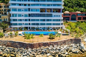 Ein mehrstöckiges Hotel mit Pool, umgeben von Felsen und Palmen.