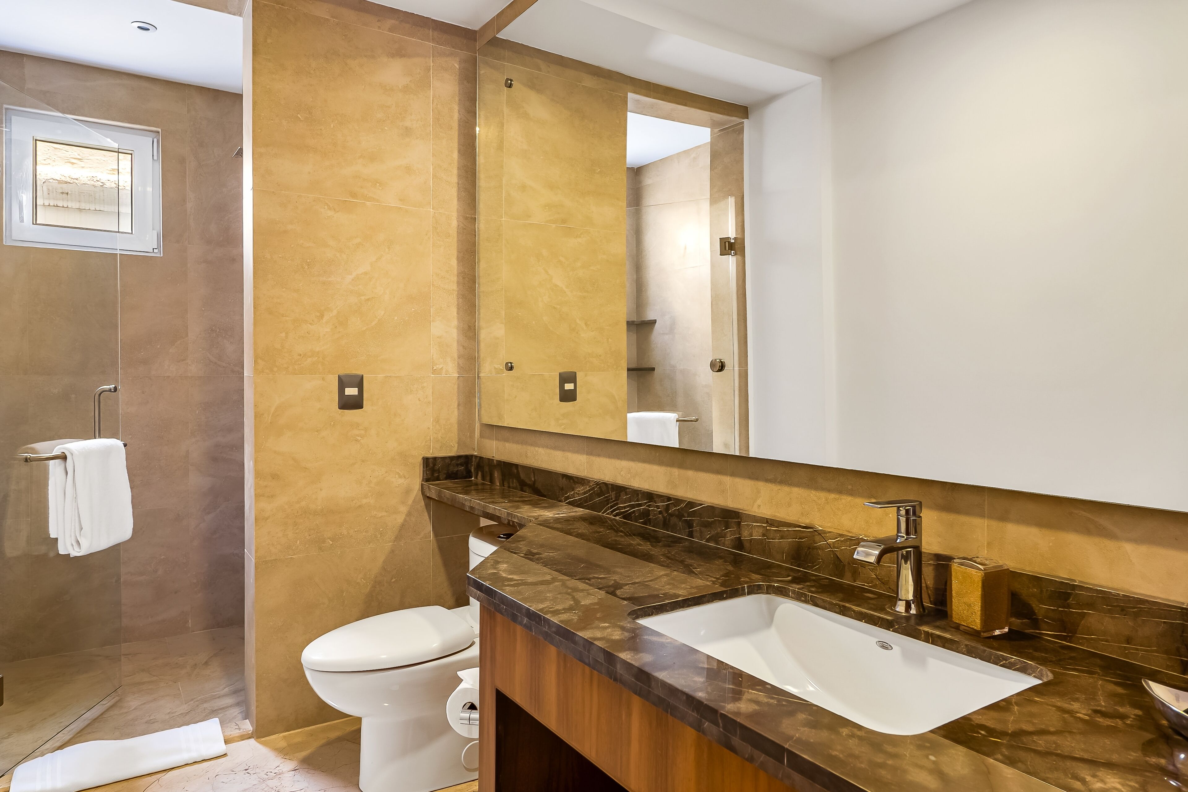 Un baño moderno con tocador de mármol, un espejo grande y zona de ducha separada.