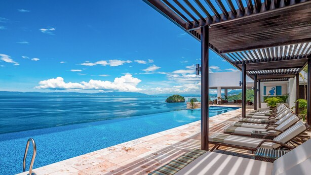 An infinity pool with a clear view of the ocean, lounge chairs, and a pergola structure. - Blue Horizon 601 | 1BR/2BA Puerto Vallarta | Ocean Views, Pool, Gym (Puerto Vallarta)